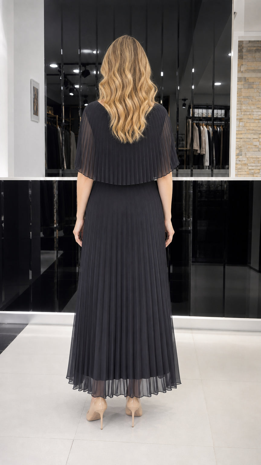 Model wearing black pleated cape overlay maxi dress, back view
