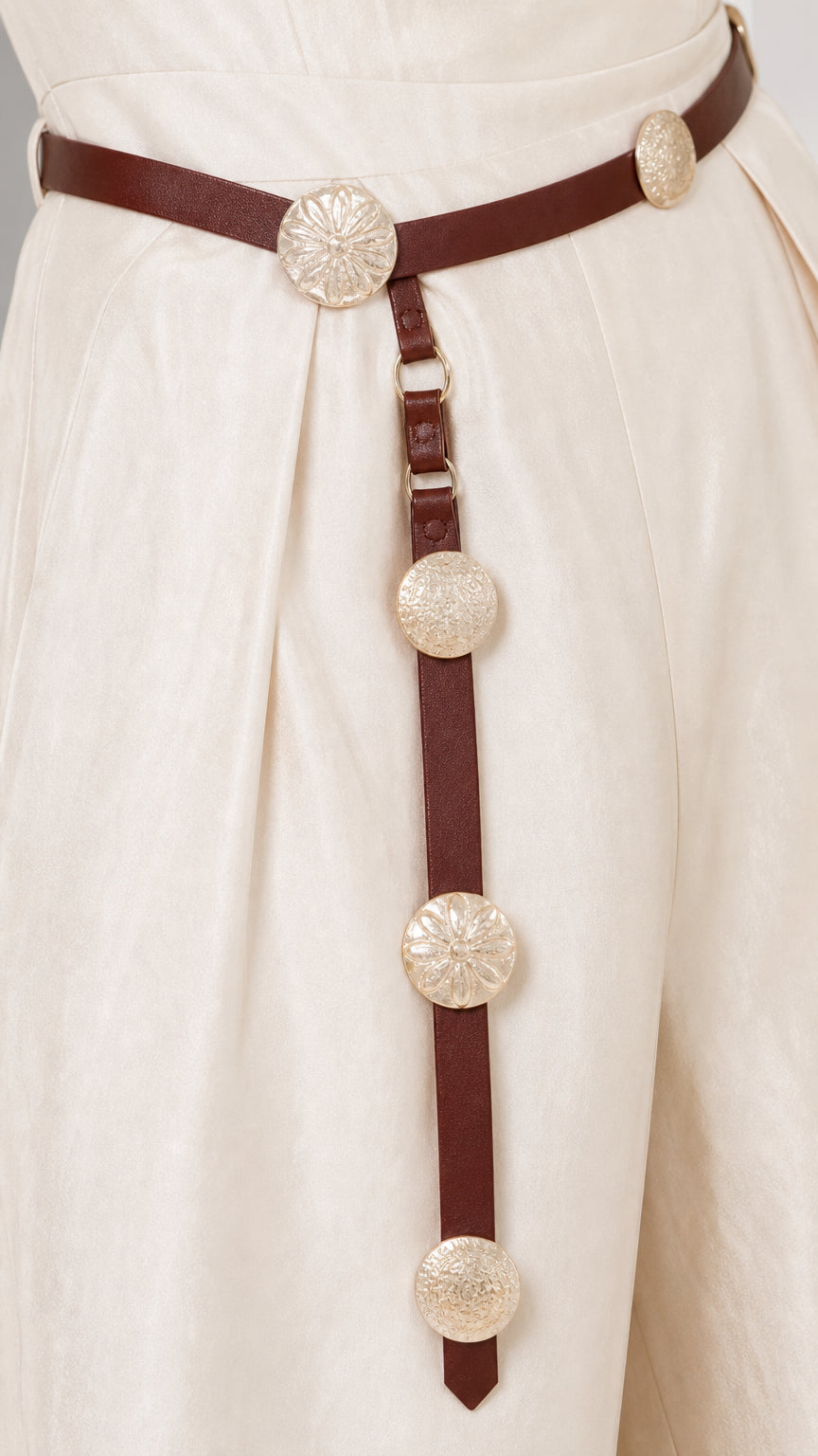 Close-up of the decorative belt with metallic medallions on ivory trousers