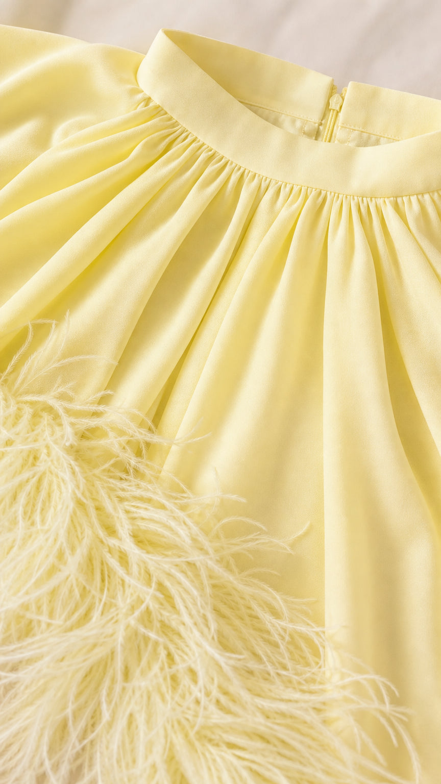 Close-up detail of yellow pleated neckline and feather hem