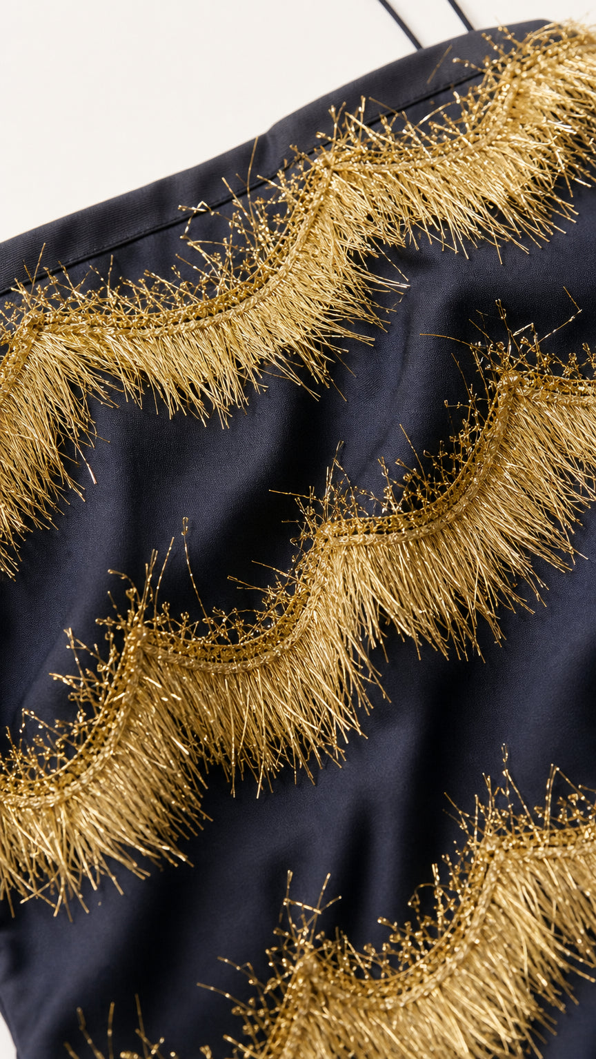 Close-up fabric detail showing gold fringe appliques on black base