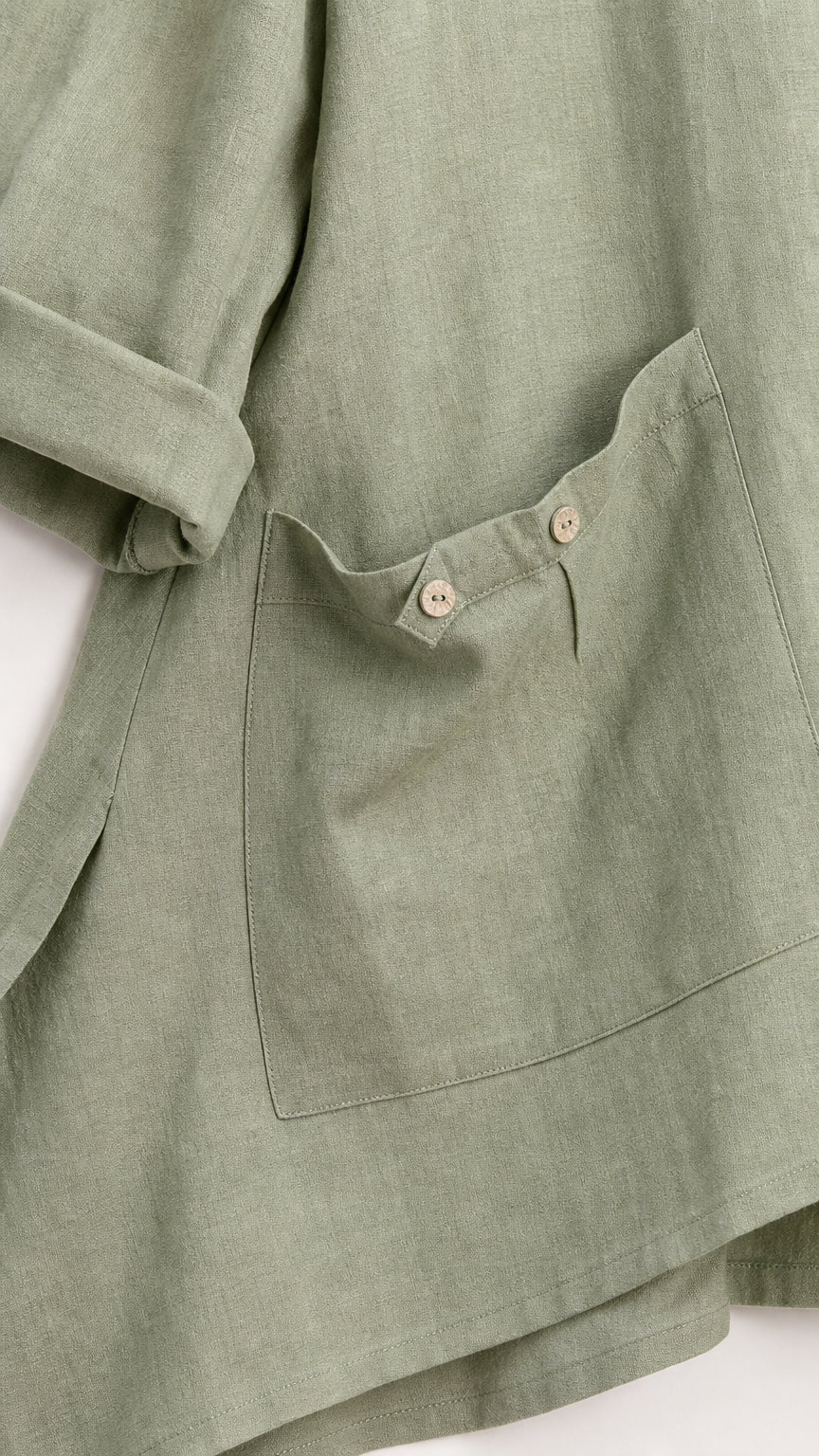 Close-up detail of tunic asymmetric hem and button pocket in sage green